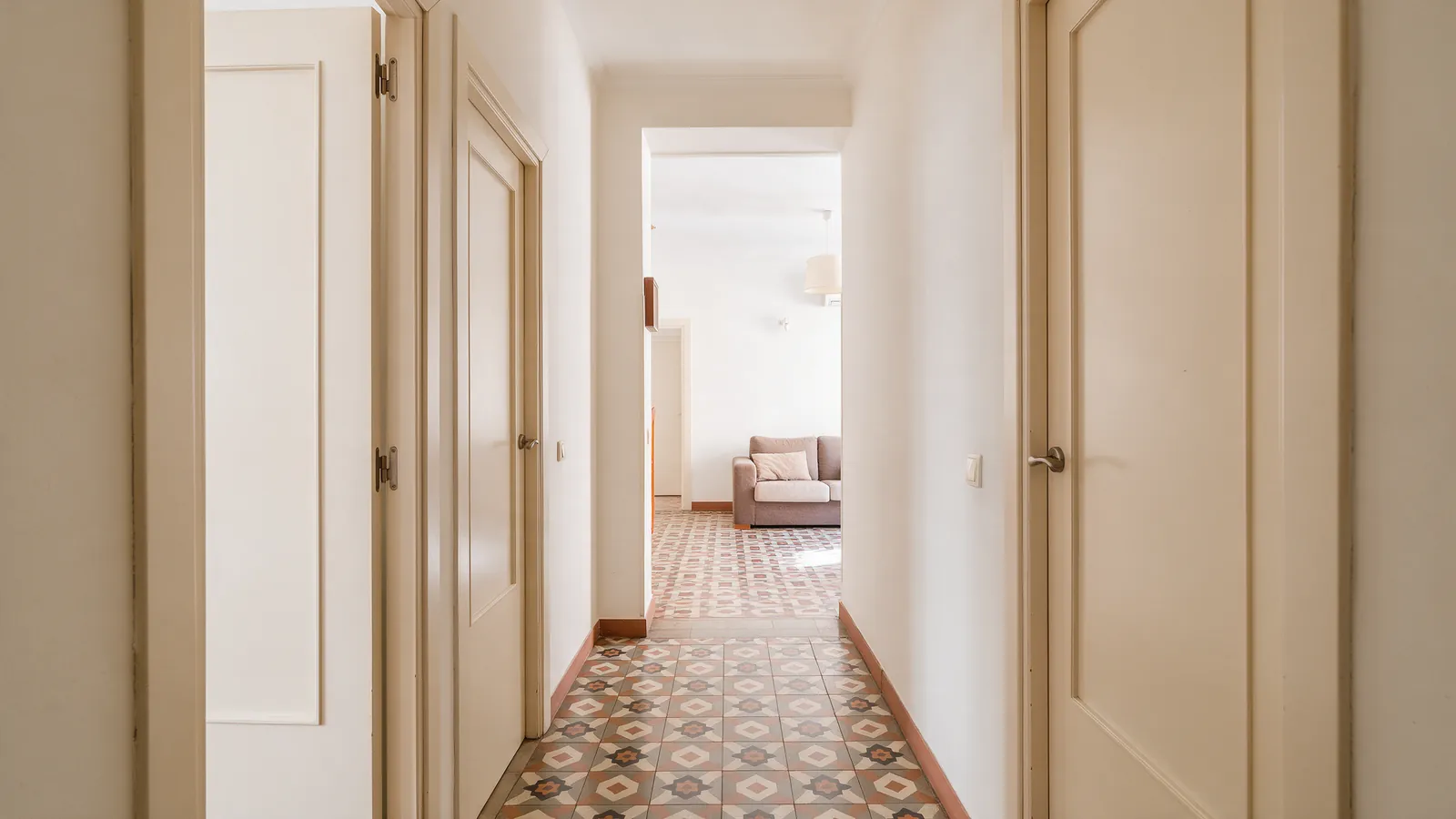 Pasillo luminoso de un piso compartido en Madrid con tres puertas de dormitorio cerradas y un salón al fondo