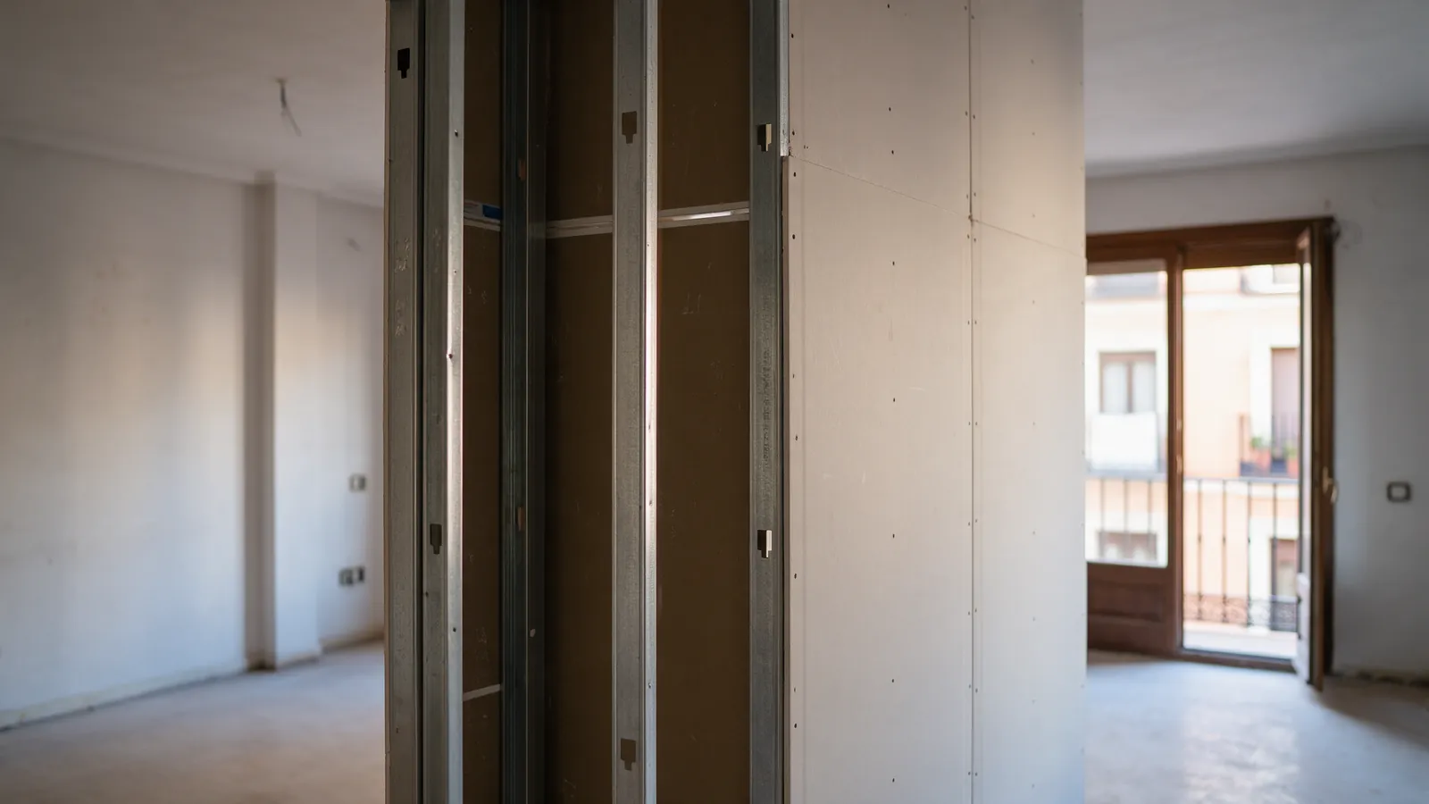 Tabique de pladur recién levantado dividiendo un salón grande en un piso de Madrid, con luz entrando solo por un lado