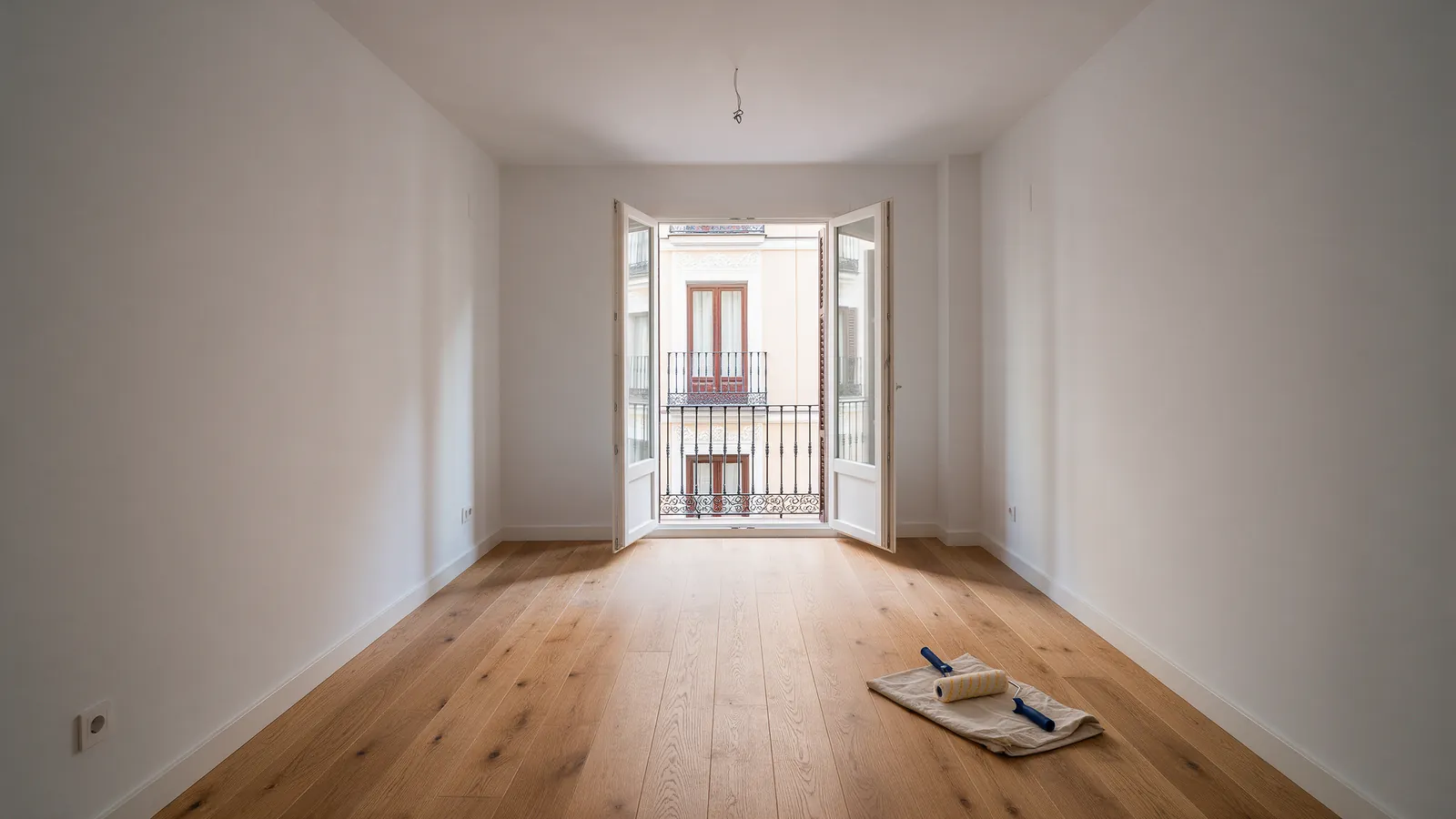 Salón de piso de Madrid recién reformado con suelo de roble claro, balcón abierto y un rodillo de pintura sobre un trapo