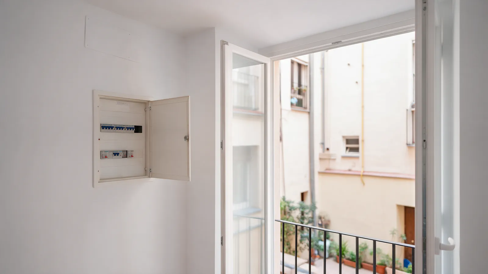 Salón luminoso reformado con ventana a un patio y un cuadro eléctrico abierto en la pared