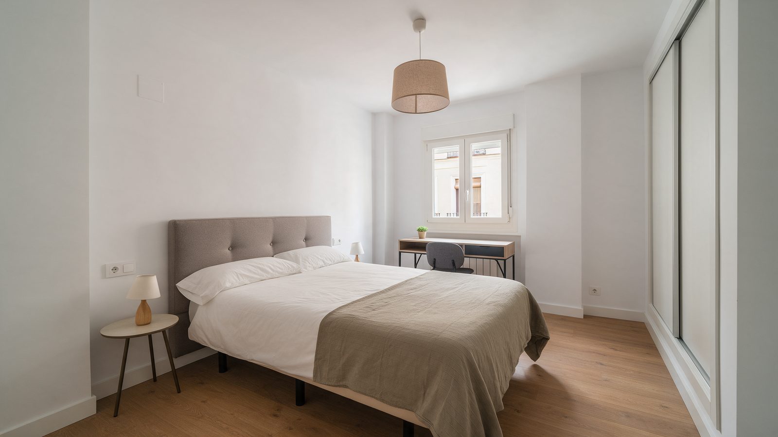 Habitación reformada y luminosa de un piso en Madrid con cama, escritorio bajo la ventana y armario empotrado