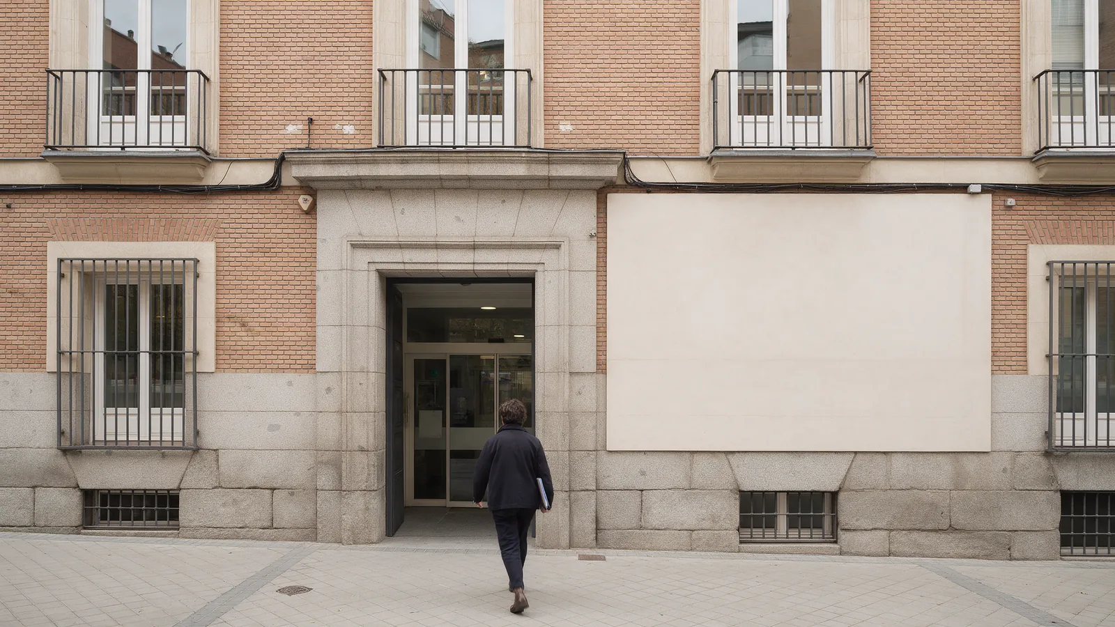 Fachada de una oficina de distrito del Ayuntamiento de Madrid con una persona entrando con una carpeta de documentos