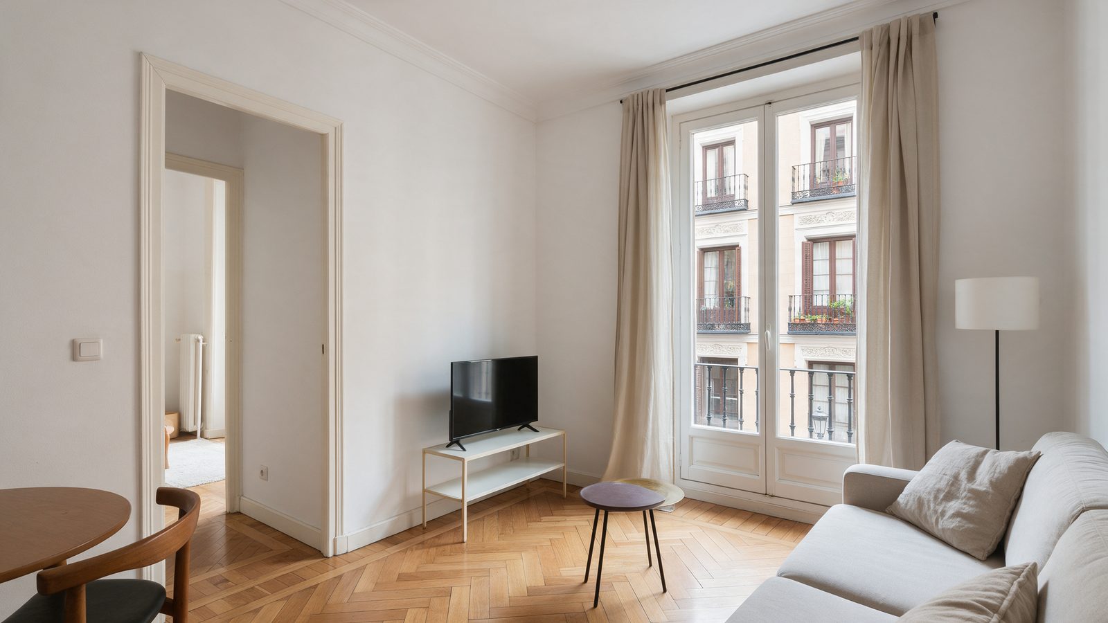 Salón luminoso de un piso de dos habitaciones en Madrid con suelo de parquet y ventanal a la calle