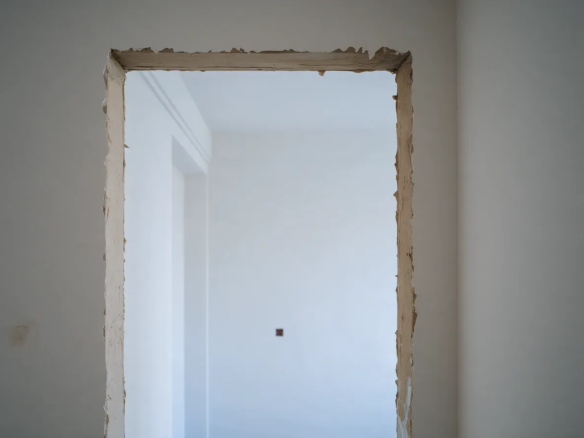 Habitación recién pintada de blanco vista a través de un marco de puerta con yeso sin acabar