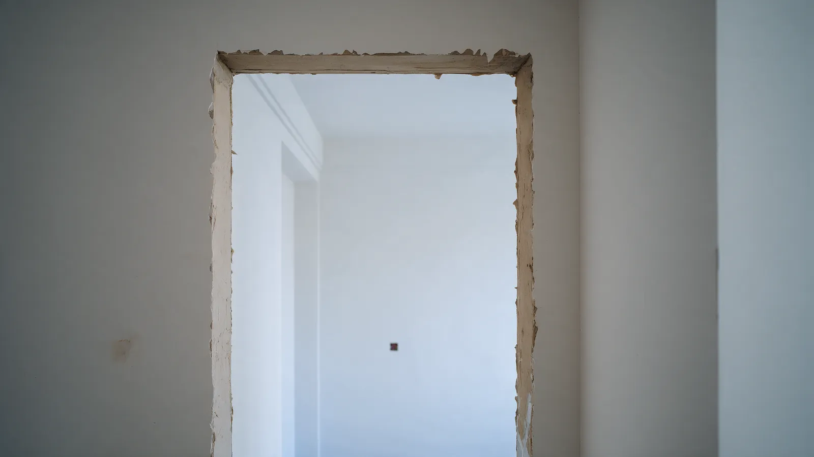 Habitación recién pintada de blanco vista a través de un marco de puerta con yeso sin acabar