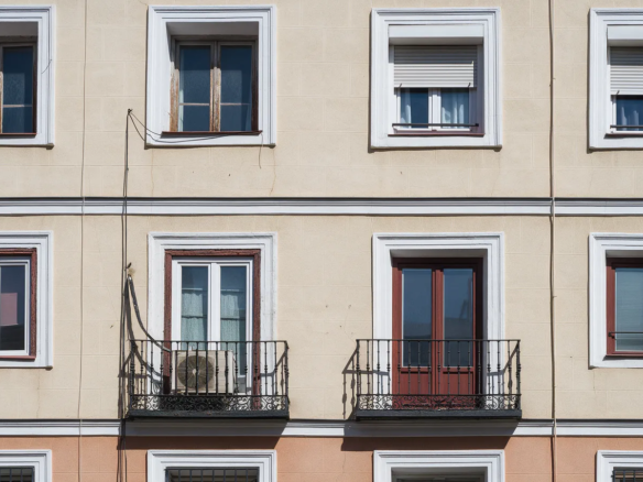Fachada de un edificio de Madrid con ventanas de distintos marcos y un aparato de aire acondicionado antiguo en un balcón