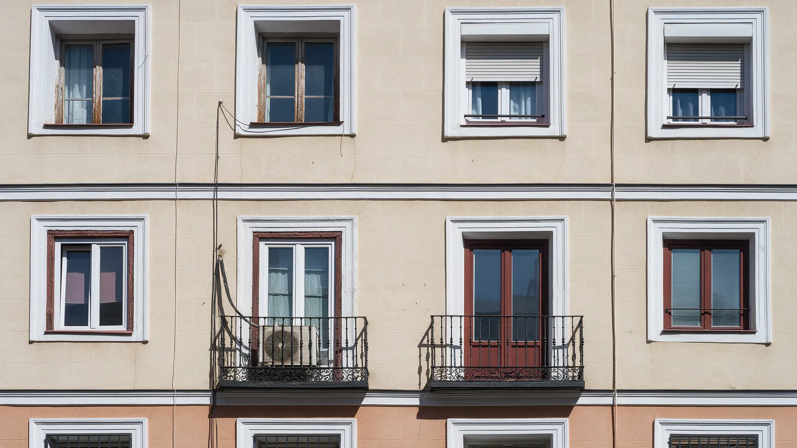 Fachada de un edificio de Madrid con ventanas de distintos marcos y un aparato de aire acondicionado antiguo en un balcón